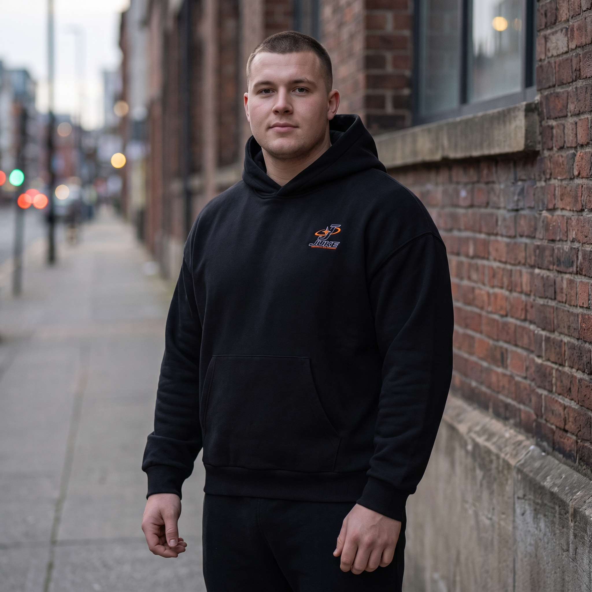 Model wearing the JUKE Unisex Drop Shoulder Hoodie on a city street at dusk